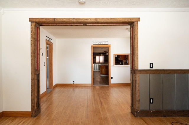 empty room featuring a textured ceiling, crown molding, wood finished floors, and baseboards