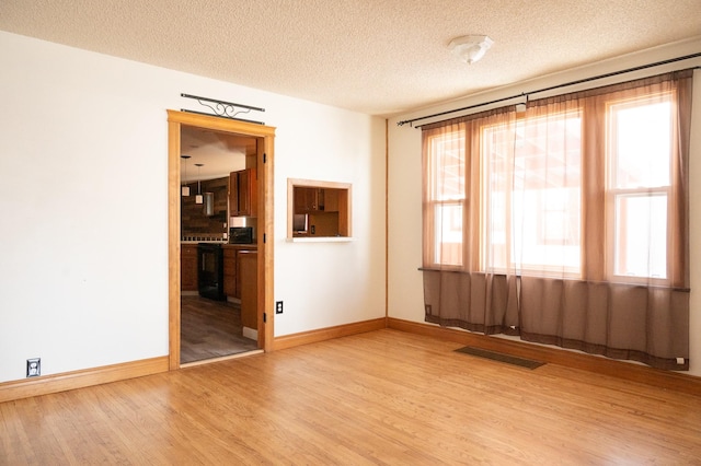 empty room featuring a textured ceiling, a wealth of natural light, wood finished floors, and visible vents