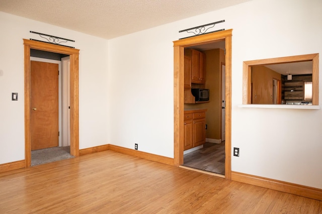 spare room featuring light wood-type flooring, baseboards, and a textured ceiling