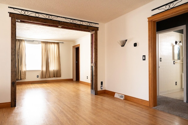 spare room featuring visible vents, a textured ceiling, baseboards, and wood finished floors