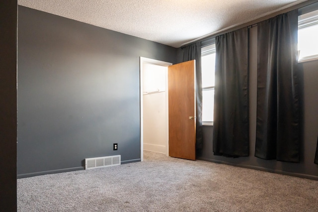 unfurnished bedroom with carpet floors, visible vents, a textured ceiling, and baseboards