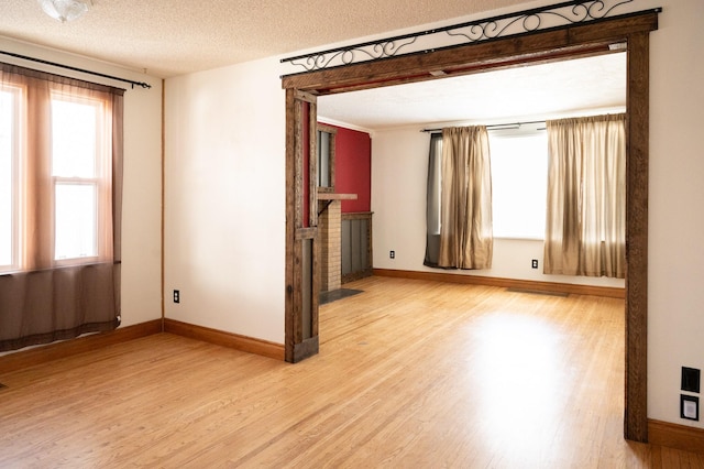 empty room with a textured ceiling, baseboards, a fireplace, and wood finished floors