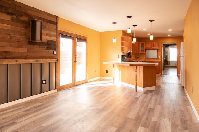 kitchen with a breakfast bar area, a peninsula, brown cabinetry, glass insert cabinets, and pendant lighting