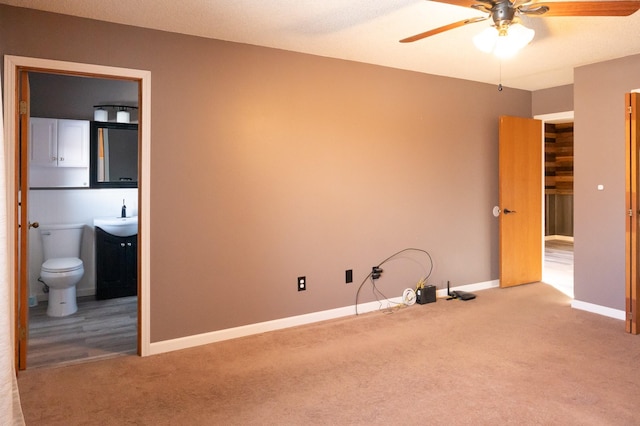 unfurnished room with carpet floors, ceiling fan, baseboards, and a sink