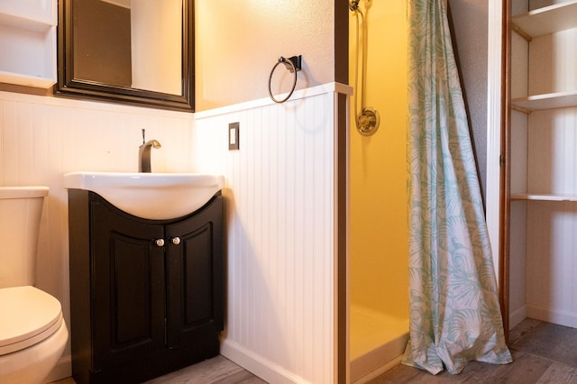 bathroom with toilet, a wainscoted wall, wood finished floors, vanity, and a shower stall