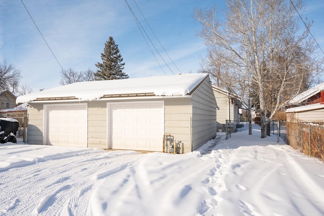 snow covered garage with a detached garage and fence