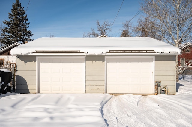 snow covered garage with a detached garage and fence