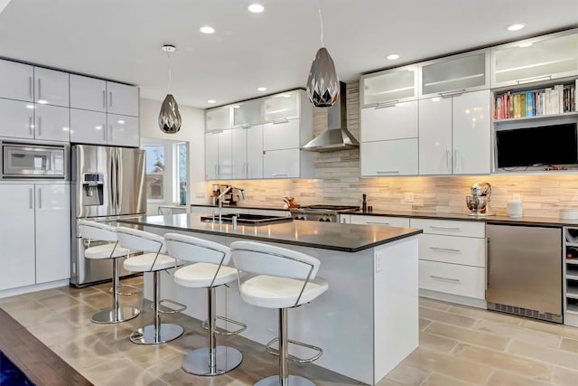 kitchen with decorative light fixtures, dark countertops, appliances with stainless steel finishes, white cabinets, and wall chimney range hood