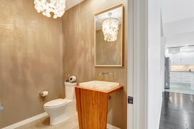 half bath featuring baseboards, a notable chandelier, vanity, and toilet