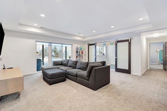 living area featuring a barn door, a tray ceiling, and light colored carpet