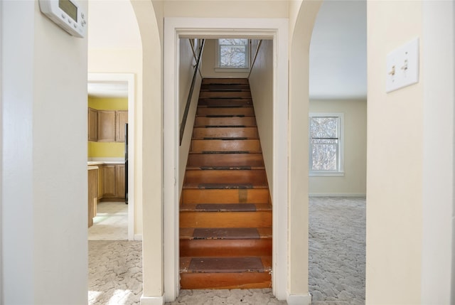 stairway featuring arched walkways, carpet flooring, and baseboards