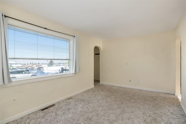 unfurnished room featuring arched walkways, baseboards, visible vents, and light colored carpet