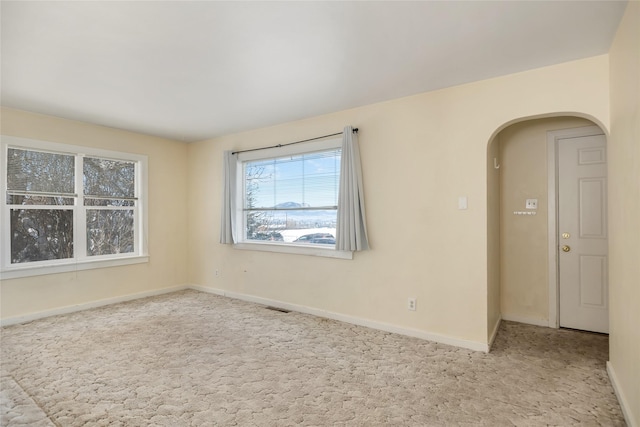 unfurnished room featuring light colored carpet, arched walkways, visible vents, and baseboards