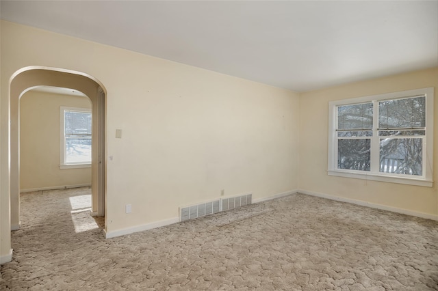 spare room with light colored carpet, arched walkways, visible vents, and baseboards