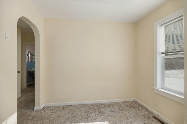 spare room with arched walkways, baseboards, visible vents, and light colored carpet