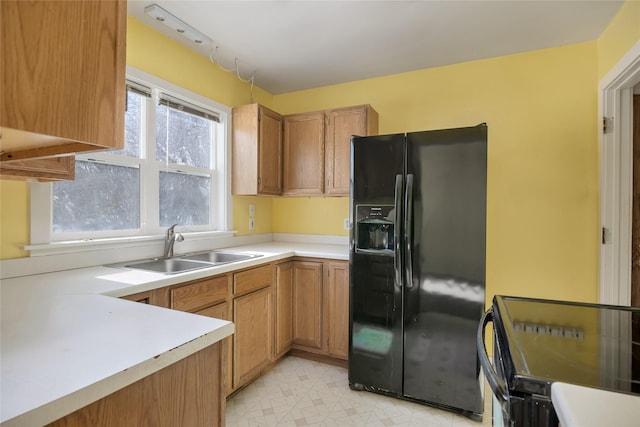 kitchen with brown cabinets, light floors, light countertops, black fridge with ice dispenser, and a sink