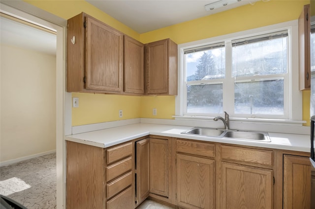 kitchen featuring brown cabinets, light countertops, a sink, and baseboards