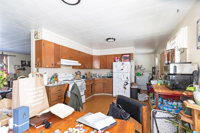 kitchen featuring under cabinet range hood, white appliances, light wood finished floors, brown cabinetry, and washer / dryer