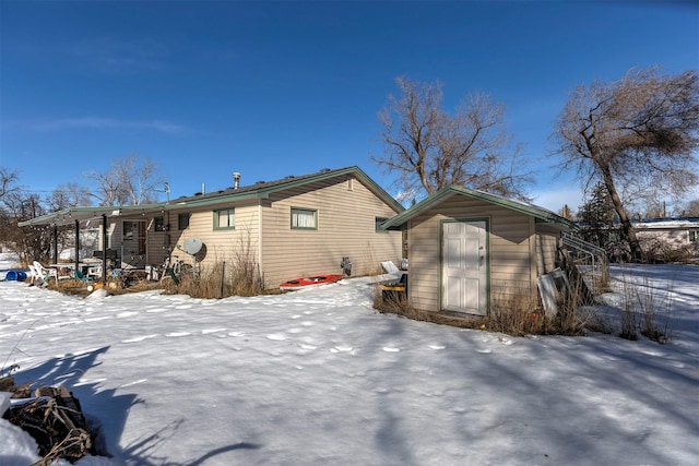 snow covered rear of property featuring a storage shed and an outdoor structure