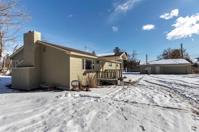 snow covered rear of property with a chimney and a detached garage