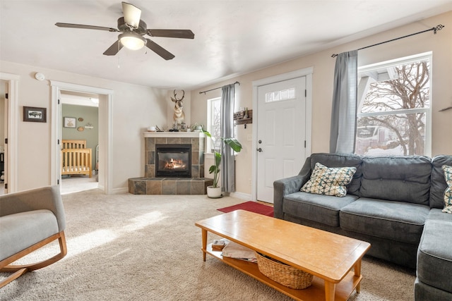 living area featuring baseboards, a tile fireplace, a ceiling fan, and light colored carpet