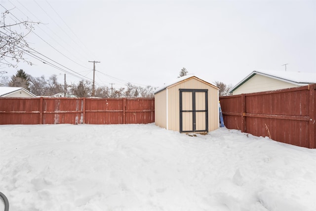 snowy yard featuring a storage shed, an outdoor structure, and a fenced backyard