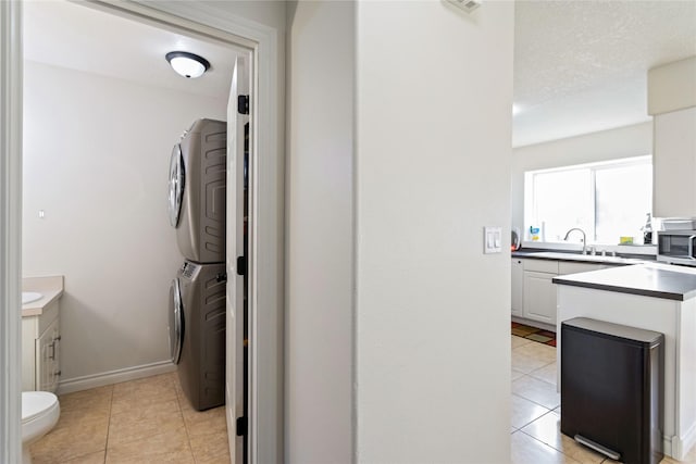 clothes washing area featuring light tile patterned floors, stacked washer and dryer, a sink, and baseboards