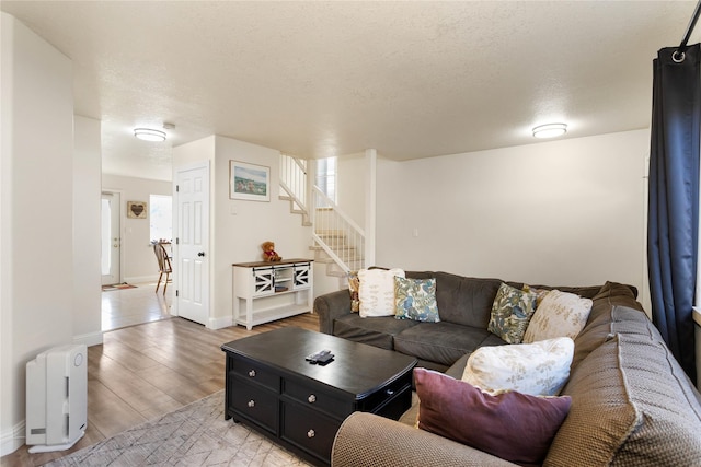 living area with light wood-type flooring, baseboards, stairway, and a textured ceiling