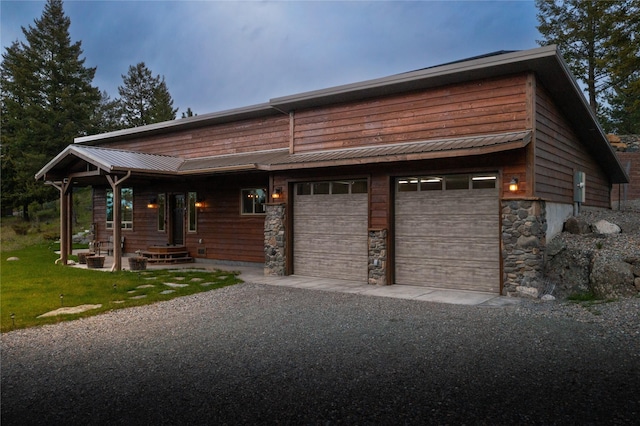 view of front of property featuring gravel driveway, stone siding, and metal roof