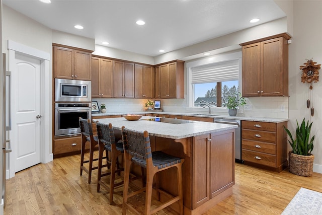 kitchen with a kitchen island, a breakfast bar, stainless steel appliances, light wood-style floors, and a sink