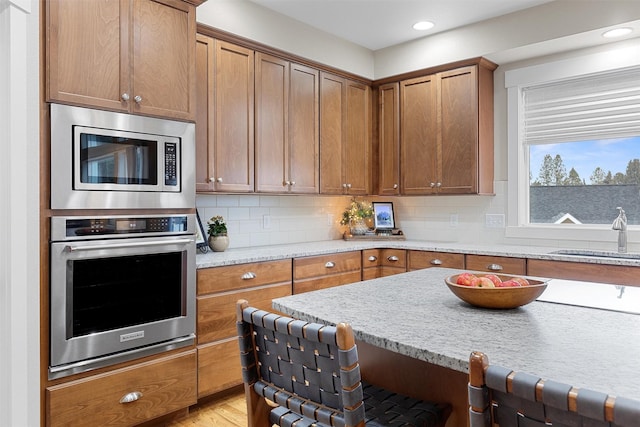 kitchen with stainless steel appliances, decorative backsplash, a sink, and brown cabinets