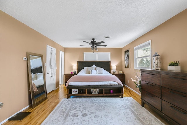 bedroom featuring a ceiling fan, visible vents, a textured ceiling, and light wood finished floors