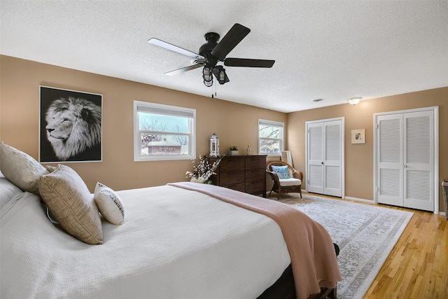 bedroom with light wood finished floors, multiple closets, ceiling fan, a textured ceiling, and baseboards