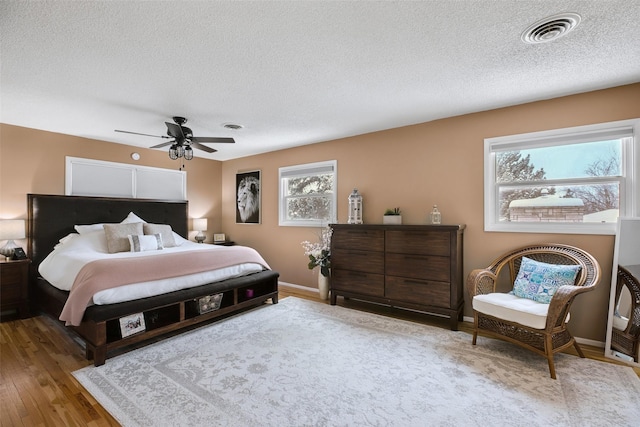 bedroom featuring a ceiling fan, visible vents, a textured ceiling, and wood finished floors