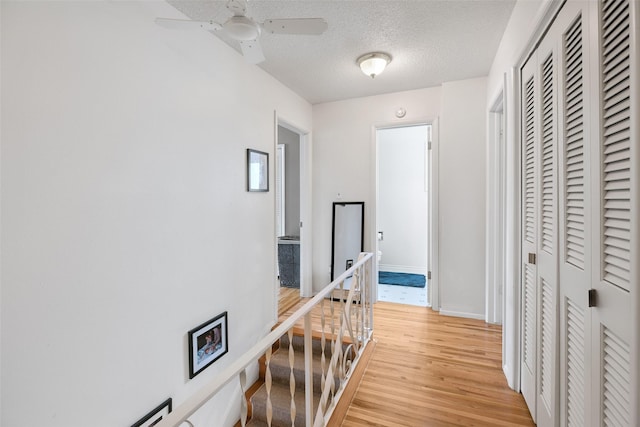 corridor with light wood-style flooring, baseboards, a textured ceiling, and an upstairs landing