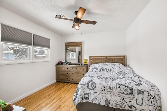 bedroom with baseboards, visible vents, ceiling fan, wood finished floors, and a textured ceiling