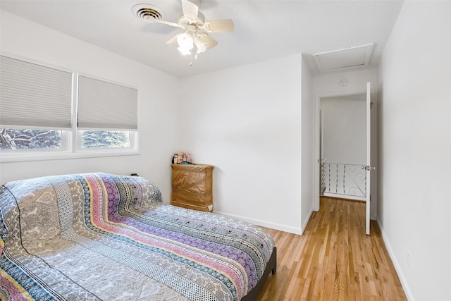 bedroom with light wood finished floors, attic access, visible vents, baseboards, and ceiling fan