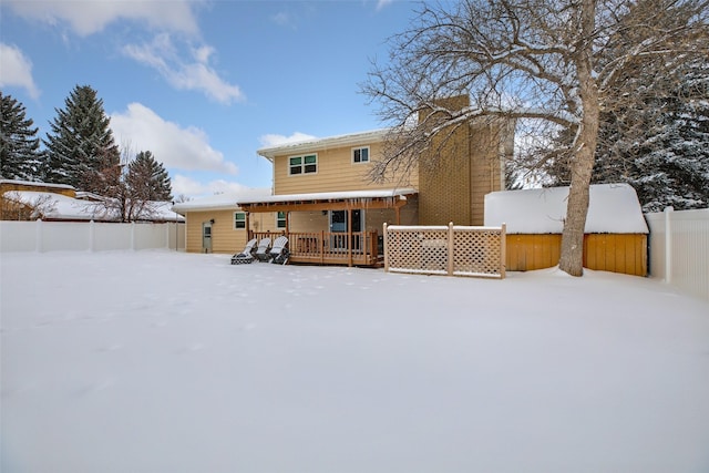 snow covered back of property with fence and a wooden deck