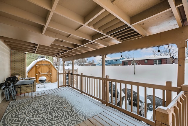 snow covered deck featuring an outbuilding, fence, and a storage unit