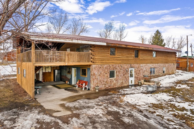 snow covered property featuring metal roof, stone siding, and log siding