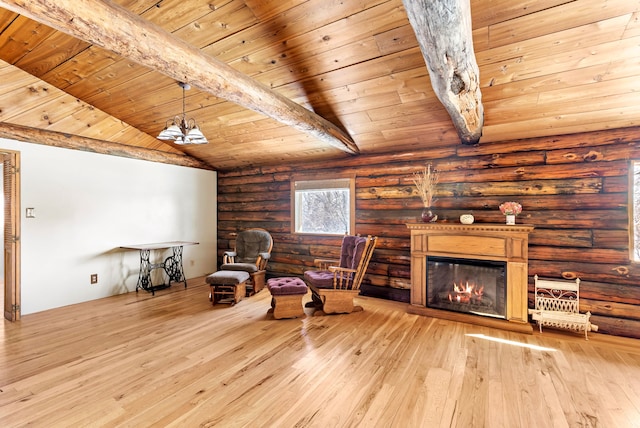 living area featuring a notable chandelier, light wood finished floors, lofted ceiling with beams, a glass covered fireplace, and wooden ceiling