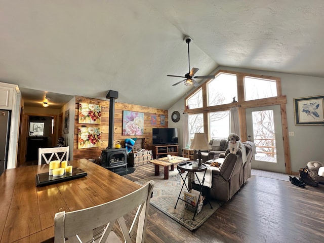 living room with a ceiling fan, hardwood / wood-style flooring, a wood stove, wood walls, and high vaulted ceiling