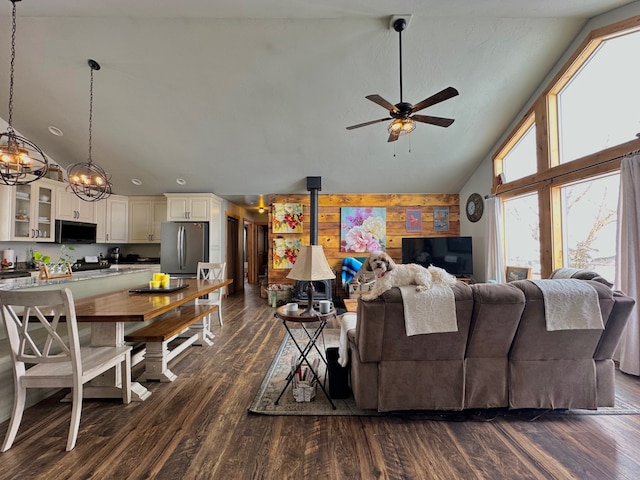 living area featuring high vaulted ceiling, dark wood-style flooring, wood walls, and ceiling fan with notable chandelier