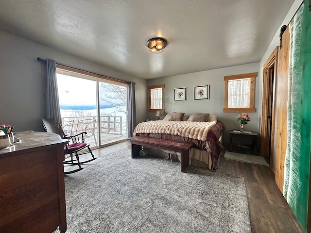 bedroom with access to exterior, a barn door, and dark wood-type flooring