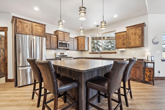 kitchen with hanging light fixtures, a kitchen island, stainless steel appliances, and a sink