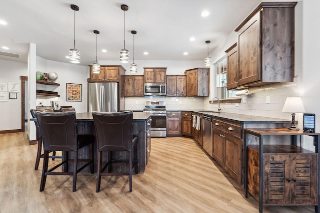 kitchen featuring a center island, decorative light fixtures, visible vents, appliances with stainless steel finishes, and a kitchen bar