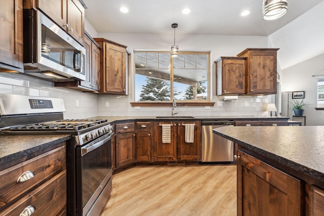 kitchen with appliances with stainless steel finishes, dark countertops, a sink, and decorative light fixtures