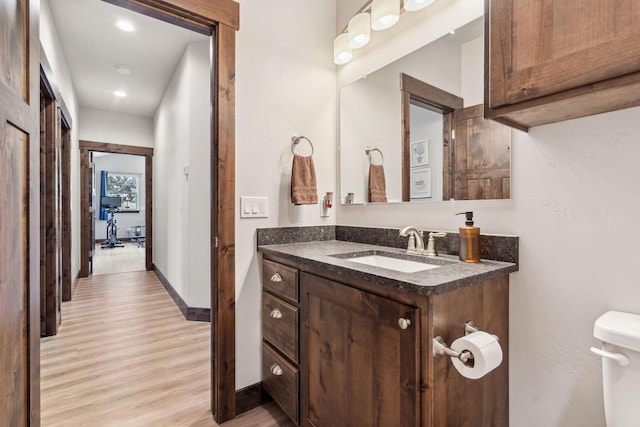 bathroom featuring toilet, baseboards, wood finished floors, and vanity