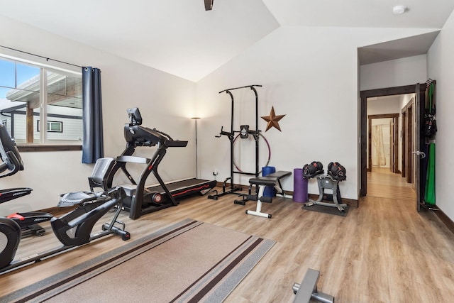 exercise room with light wood-type flooring, vaulted ceiling, and baseboards