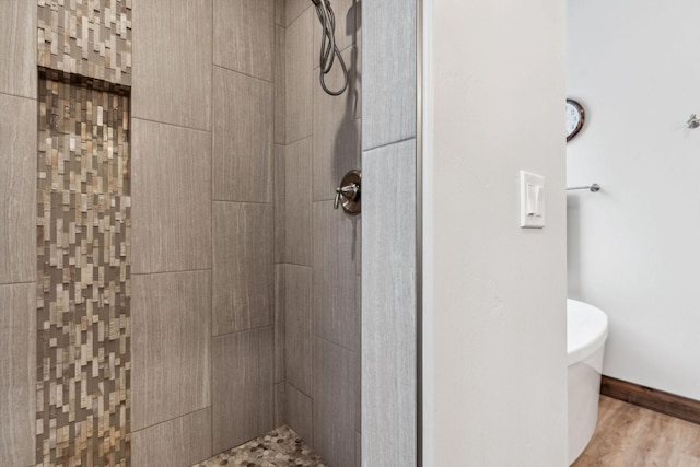 bathroom featuring toilet, a tile shower, and wood finished floors